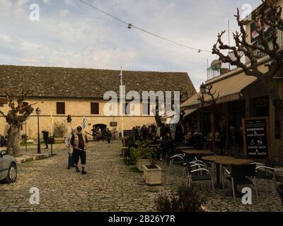 View along cobbled street to entrance to Monastery of Holy Cross with visitors sitting out in restaurants on warm February day in attractive mountain Stock Photo