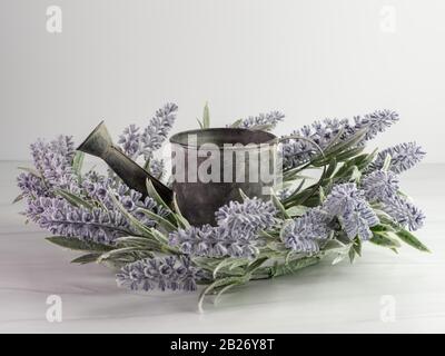 Purple lavender flower wreath surrounding a rustic metal gray watering can.  Indoor spring home decor on a white background. Stock Photo