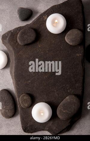 Frame made out of and black round smooth zen stones on black rough flat stone with white spa candles. Copy space. Stock Photo