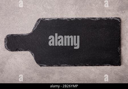 Flat lay view of natural rough black rock serving board  on gray textured surface for background. Stock Photo