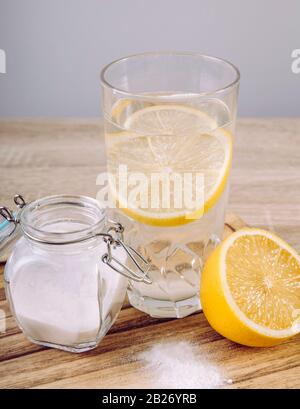 Baking soda in drinking glass with water and lemon juice, health benefits for digestive system concept on natural wooden background. Stock Photo