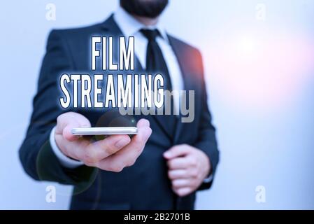 Handwriting text Film Streaming. Conceptual photo act of watching sound or video directly from the internet Male human wear formal work suit hold smar Stock Photo