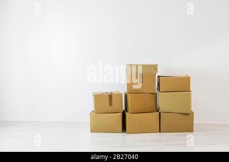 Pile of cardboard boxes against empty white wall on white flooring, with lot of copy space. Moving service concept. Stock Photo