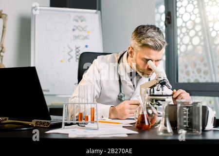 Senior Caucasian male scientist working with laptop, test tubes and flasks at the modern laboratory. Man scientist working in pharmaceutical Stock Photo