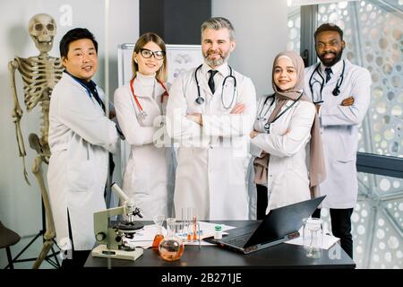 Smiling multiethnic group of doctors, scientists in modern laboratory with senior male leader. Team of young doctors residents or students with mature Stock Photo