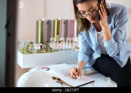 architect in stylish clothes doing work in her studio, small model of building in the background of the photo. close up photo. blurred background , fe Stock Photo