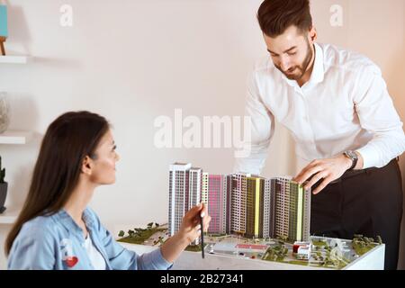 cheerful bearded man in white shirt and black pants showing small model of new buildings to his boss, presentation concept. close up photo Stock Photo
