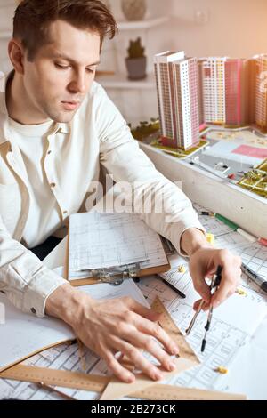 It is all about accuracy. Close-up of young serious blonde man concentrated on using compass for drawing. close up photo. vertical shot.concentration Stock Photo
