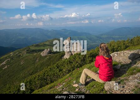 Girl in bright clothes sits and contemplates the mountains. Stock Photo
