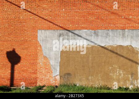 an exterior red and orange brick wall with grass verge on a bright sunny afternoon with lamp post casting shadows Stock Photo