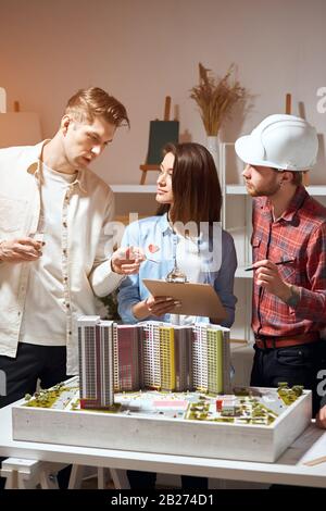 blonde handsome man sharing with his ideas with a woman and a man, they are talking about future construction, close up photo. conversation with partn Stock Photo