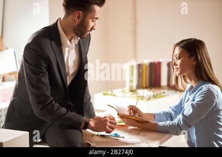 woman in glasses writing something on the notepad while man is sitting on the table and giving instructions to her. close up side view photo Stock Photo