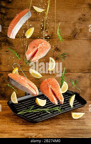 Fresh salmon or trout fish with spices and herbs falling on grill pan on wooden background. Flying food and levitation concept. Stock Photo
