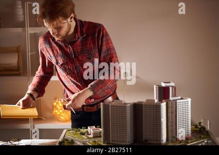 young man in stylish checked shirt hoilding a pen and notepad and looking for necessary architectural tools. close up photo Stock Photo