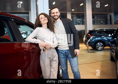 awesome young couple repare to travel Handsome young bearded smiling man embracing his beautiful girlfriend at the car dealership happy woman smiling Stock Photo