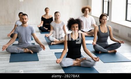 Diverse young people seated cross-legged practicing meditation together indoors Stock Photo