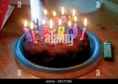 A home-made cake on a plastic plate with lighted candles spelling the words 'Happy Birthday' at a child's party Stock Photo