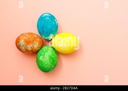 Four multi-colored Easter eggs on pink background top view, space for text. Concept happy easter day. Stock Photo