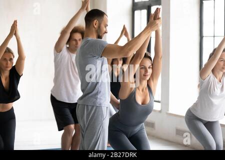 Male yoga instructor helping to woman do right Utkatasana position Stock Photo