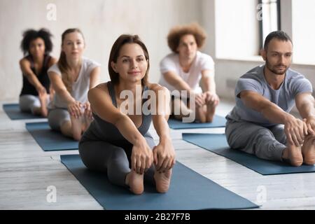 Diverse group of people doing Seated Forward Bend or Paschimottanasana Stock Photo