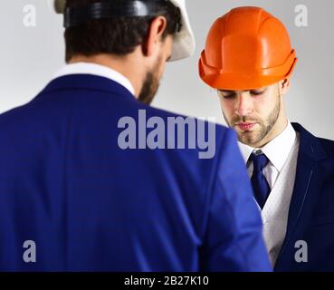 Construction, business people, architecture concept. Engineers with serious faces. People in helmets isolated on white background. Architects think about project. Businessman and engineer back view. Stock Photo
