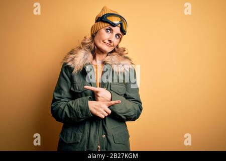 Middle age beautiful blonde skier woman wearing snow sportwear and ski goggles Pointing to both sides with fingers, different direction disagree Stock Photo