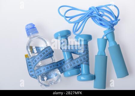 https://l450v.alamy.com/450v/2b27mfk/fit-shape-and-sport-concept-dumbbells-skipping-rope-in-cyan-color-near-water-bottle-on-white-background-health-and-fitness-symbols-jump-rope-water-and-barbells-tied-with-blue-measure-tape-2b27mfk.jpg