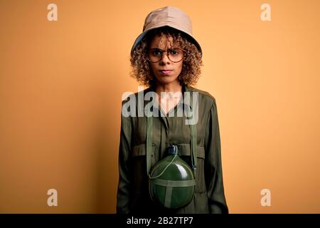 Young african american tourist woman on vacation wearing explorer hat and water canteen skeptic and nervous, frowning upset because of problem. Negati Stock Photo