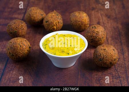 Tahini sauce made with turmeric powder, garlic and minced parsley leaves, in a white bowl. Vegan chickpea falafel placed around the bowl. Stock Photo