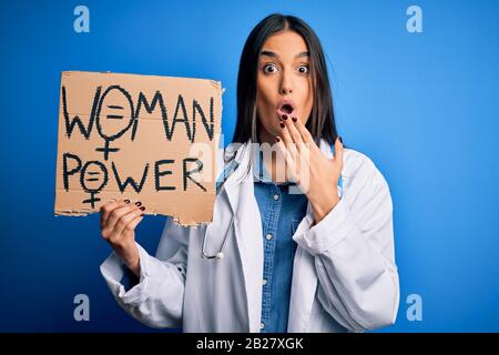 Young doctor woman wearing stethoscope holding cardboard banner with powe message cover mouth with hand shocked with shame for mistake, expression of Stock Photo