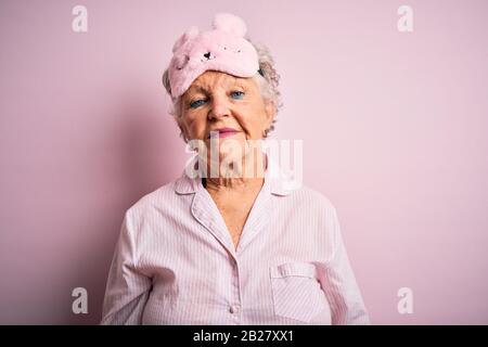 Senior beautiful woman wearing sleep mask and pajama over isolated pink background Relaxed with serious expression on face. Simple and natural looking Stock Photo