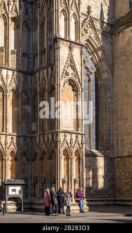 The west tower of York Minster caught in a winter sun.  A group of people are dwarfed by the tower’s wing as they stand in the sunshine. Stock Photo