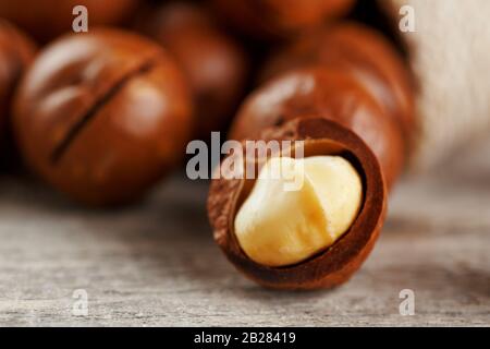 Macadamia nuts spilled out of the bag on a wooden background close-up with one peeled nut Stock Photo