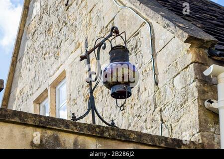 A vintage oil lamp converted  to electric made of metal and a red glass globe well patinaed with green hanging from a bracket from a wall next to a ho Stock Photo
