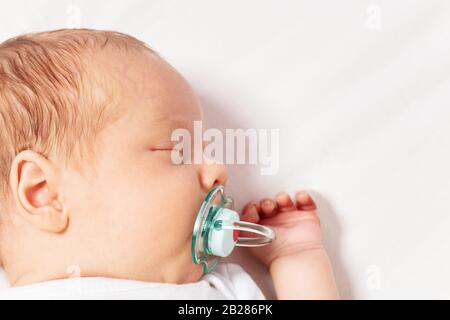 Face close-up portrait of newborn infant baby boy laying on the bed with pacifier sleeping Stock Photo