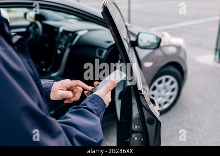 Male hands typing on cell phone. Unrecognizable mature man standing at rental car with smartphone. Stock Photo