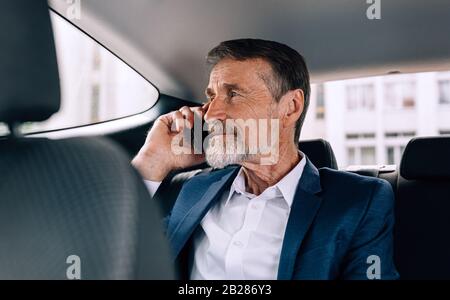 Pensive senior man holding a cell phone and looking on window while sitting in car Stock Photo