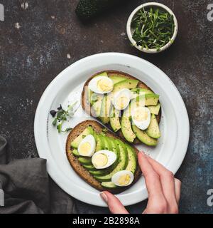 Hand picking avocado and quaill egg rye bread toast. Healthy food, clean eating concept Stock Photo