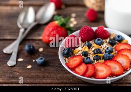 Granola with blueberries and raspberries in white bowl in dark wooden desk. Stock Photo