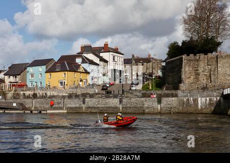 RNLI inshore rescue boat approaching Cardigan bridge, going up river Teifi on emergency call out, with Cardigan town and castle in the background. Stock Photo