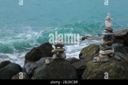 Stone cairn on seacoast in front of wave. Big rocks and balanced pebbles stack. Relaxation, harmony, balance concept. Stock Photo