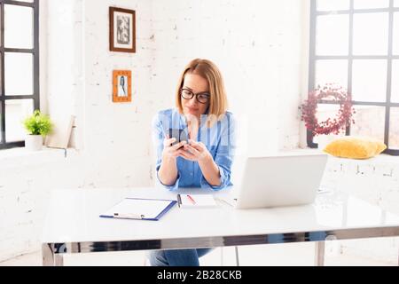 Shot of smiling businesswoman text messaging while sitting behind her notebook and workin in the office. Stock Photo