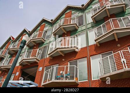 Perspective view of a red brick and green wood three stacked apartment complex with small individual patio balconies and with multiple pitched roof po Stock Photo