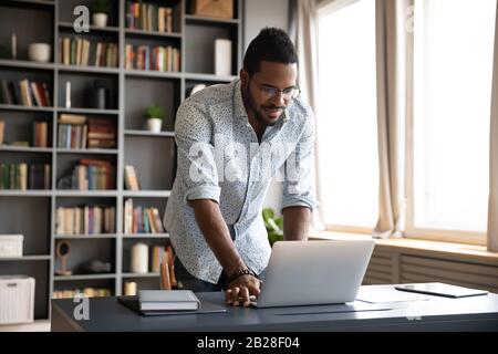 Happy young biracial freelance man working standing at table. Stock Photo