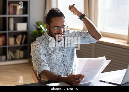 Overjoyed young mixed race businessman celebrating good offer contract. Stock Photo