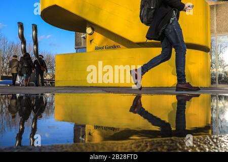 London, UK. 1st Mar, 2020. Visitors to London's Southbank Centre are reflected in rain puddles as they walk past one of the centre's iconic bright yellow brutalist architecture staircases. The day in London saw beautiful sunshine with blue skies, in stark contrast to Saturday's rain and storm. Credit: Imageplotter/Alamy Live News