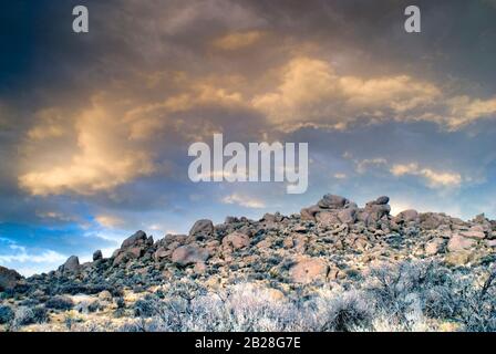 Rocky Hilltop in the High Owyhee Desert under a Front-Lit Sky of Clouds in a Paralleled curve shape during a sunset in Idaho Stock Photo