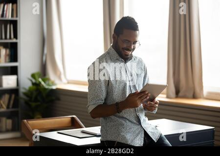 Smiling businessman web surfing information at home on digital tablet. Stock Photo