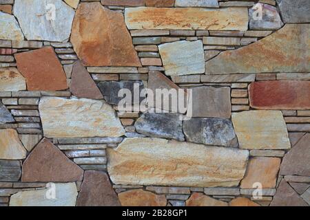 Multy-colored (colorful) decorative stone wall, texture, background. Varicolored natural stones in the wall construction. The fragment of tessellated Stock Photo