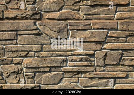 Beige-colored decorative stone wall, texture, background. Tan or light-brown stones of irregular shape in the wall construction. Decorative stones Stock Photo